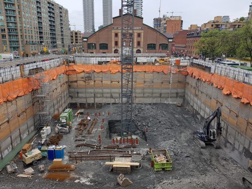 excavation and shoring nearing completion, tower crane installation underway.