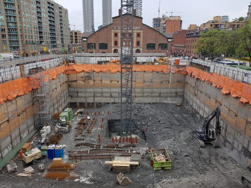 excavation and shoring nearing completion, tower crane installation underway.