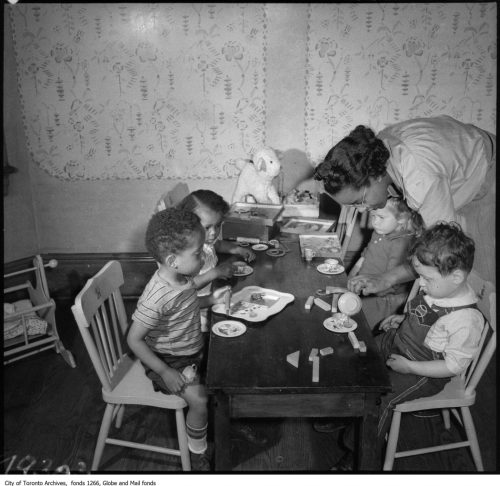 Children seated around table eating, at nursery, with teacher