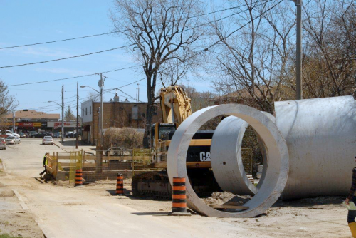 An oversized pipe on a street, with a traffic cone in front of it for comparison