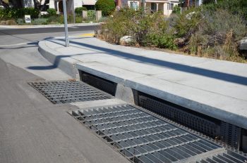 Large grated catch basins near the edge of a motor vehicle road and side of the sidewalk