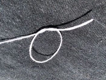 The beginnings of tying a knot in thread that's been threaded through a needle