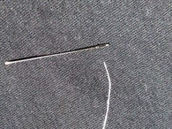 A white thread laying next to the needle on fabric