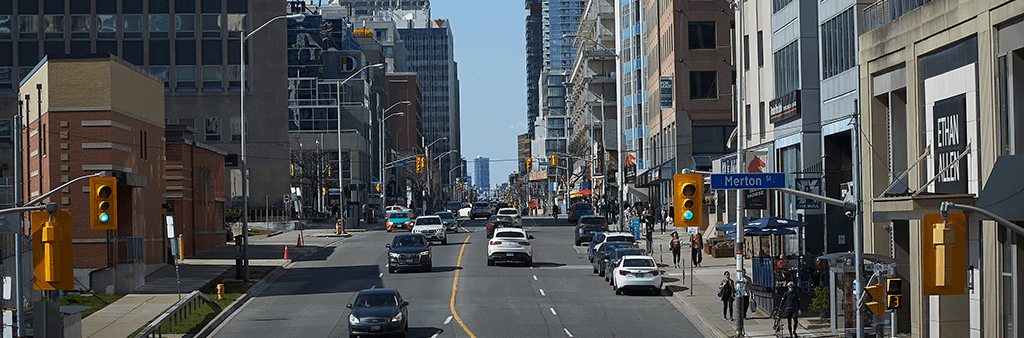 A photo of Yonge Street near Merton Street looking north, showing traffic, pedestrians, and mixed-use development along the street.