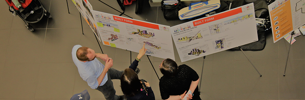 Members of the public pointing to a display board during a public meeting event.