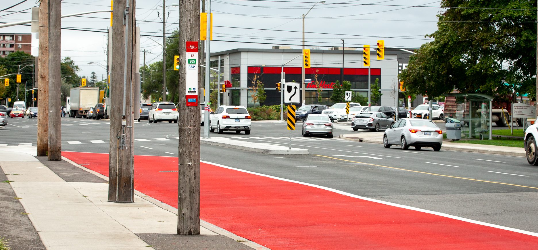 Image of Eglinton showing 4 lanes of traffic. The curb side lanes in each direction are painted red to indicate that only buses are allowed to use the lane. 