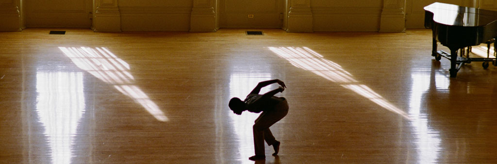 Person dancing in a sunlit gymnasium.