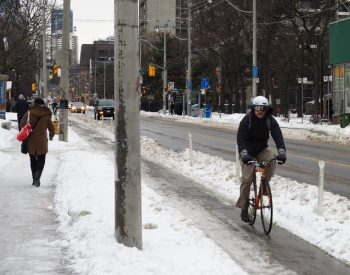 Photo showing a cyclist using a cycle track with snow stored at the curb and in the buffer