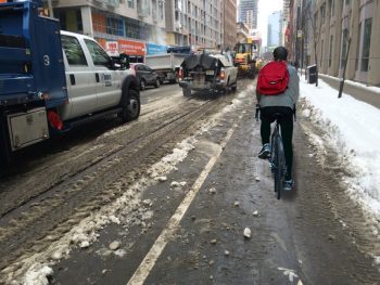 Photo showing a buffered bike lane with a cyclists and snow piled at the curb.