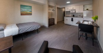 View of an apartment in 11 Macey Ave. Single bed, chair, dresser, kitchen and dinning table. 