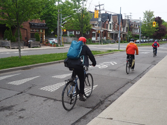 Three cyclists going over a speed bump, approaching an intersection on an overcast day.