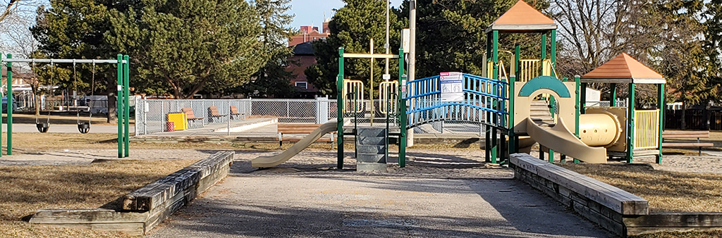 An image of the playground at Plunkett Park which includes one combined junior/senior play structure with various climbing features and slides. The playground and swing set are on sand play surfacing and grass surrounds most of the playground.