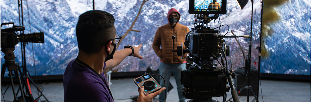 Image of film shoot taken from behind the camera, with technician directing actor.