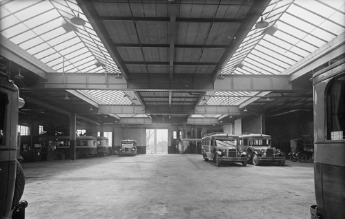 The interior of a large garage with two long skylights in the roof. There are several small buses parked along the sides.