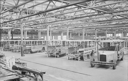 A large factory with a row of buses in different states of completion. One has a bus body on wheels, but others are just metal shells waiting for wheels and interior fixtures..