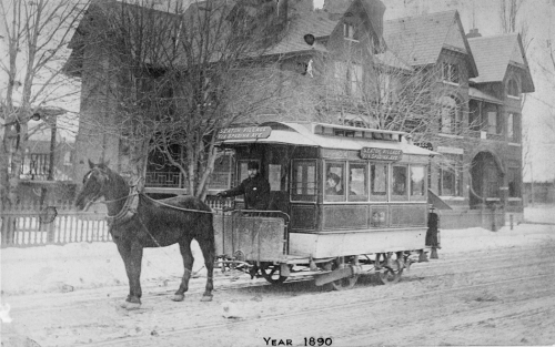 A small streetcar pulled by one horse. The driver is outside on a platform at the front of the car. 