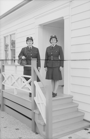 Two uniformed women standing on stairs by white one storey building.