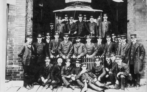 A group of men in uniforms poses in front of a streetcar at the door of a garage.