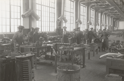 A large room with enormous windows. Workers are repairing machinery at tables.