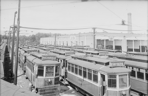 Several rows of streetcars in front of a large brick garage.