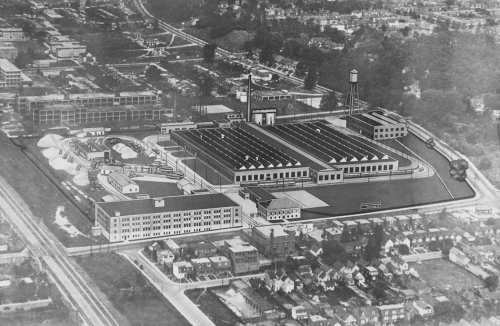 An industrial complex, including two long, low buildings with clerestory windows, a four-storey office building, a streetcar track loop, and a water tower.