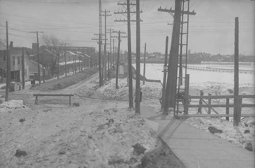 A large open space containing only a few fences. It is covered in snow. It is bordered by roads with houses on them. I