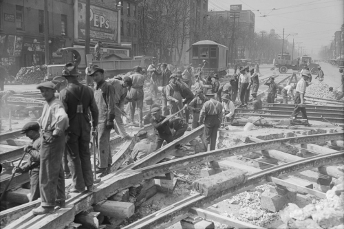 Many men digging the road up around a network of streetcar tracks.