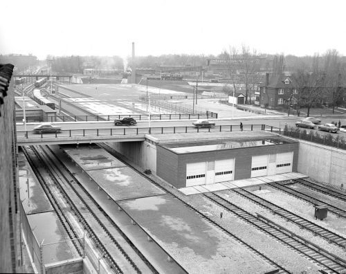 Subway tracks and a brick garage with four doors sit under a bridge.