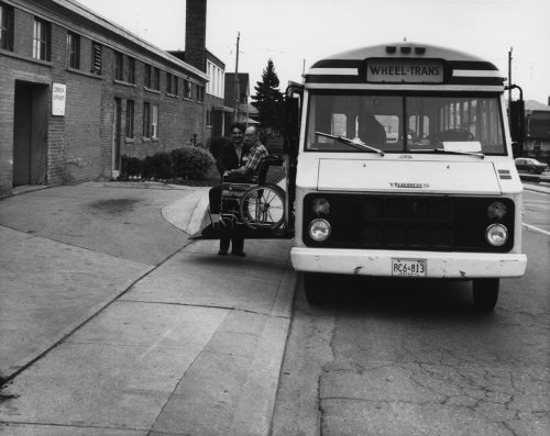 A man is sitting in a wheelchair on a ramp extending from the side of a bus.