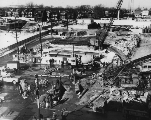 Heavy machinery including cranes and cement trucks with construction crew and construction supplies hoarding is installed around site