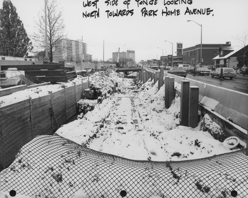 Snow covered excavated trench for subway tunnel with traffic on Yonge Street.