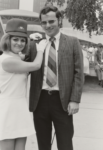 Uniformed women posing with a man for the camera. Woman is wearing a white mini dress. The man is in a suit.