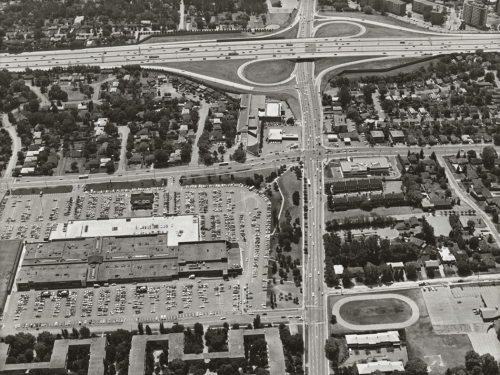 Foreground shows mall, parking lot, and subdivisions. Background shows highway and subdivisions.