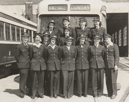 Thirteen uniformed women standing in front of streetcar in yard.