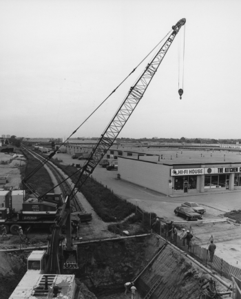 Crane and excavator preparing for excavation beside one story complex.