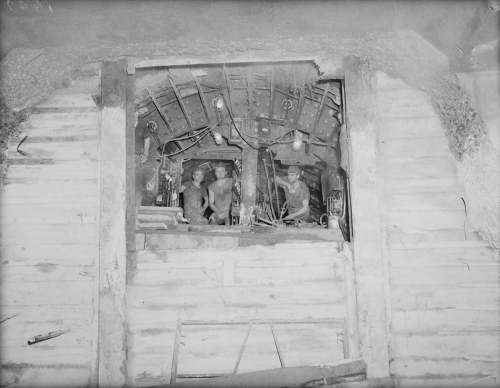 Three men looking through hole to larger excavated area.