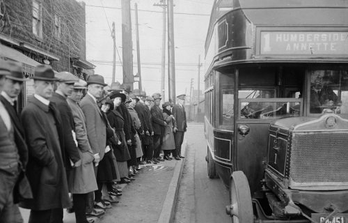 A line of people are standing along a curb waiting to board a bus.