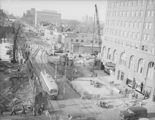 PCC on streetcar tracks at lights, traffic, in background heavy machinery in operation between buildings.