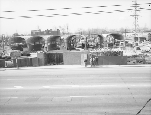 Looking towards hoarding for station construction. Four workers stand in front of hoarding.