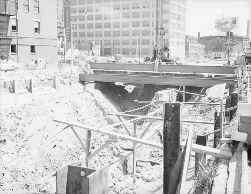 Cross section showing excavation under road decking being placed at road and multi-storied buildings in the background