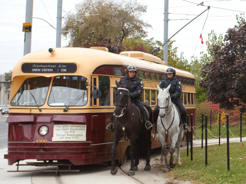 Two police on brown and white horses ride beside a red and yellow painted streetcar.