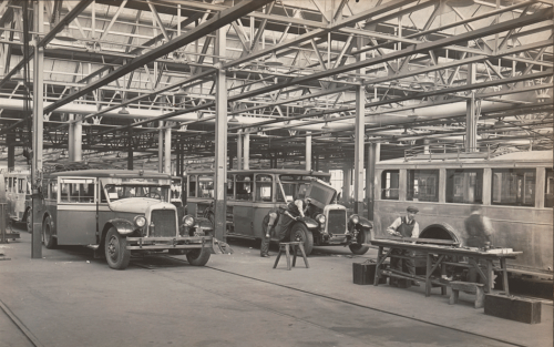 Carpenters are replacing sections on the sides and fronts of small buses in a larger room.