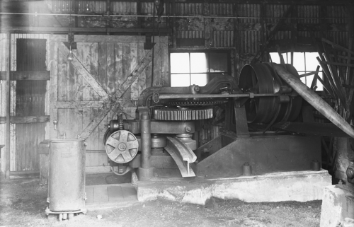 A large machine with many cogs and wheels. A piece of metal streetcar track shaped like an I-beam is sticking out of it.