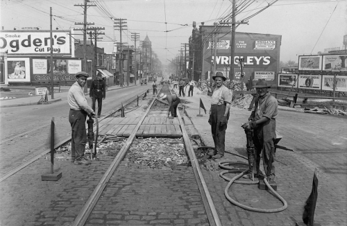 Men with jackhammers are breaking up the brick road around streetcar tracks.