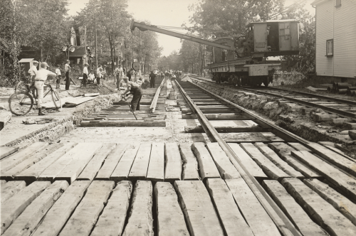 Large square timbers are laid in rows between streetcar tracks on a road.