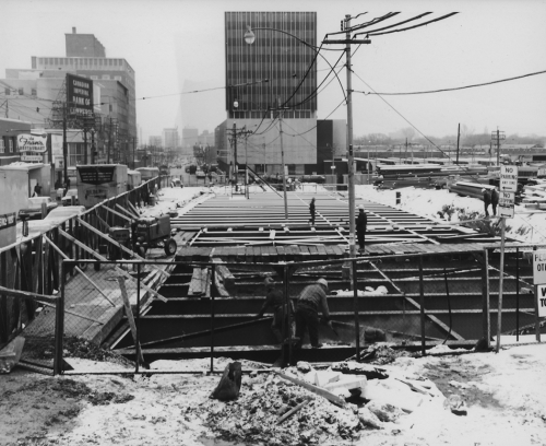 Snow covered beams with hoarding on far side of construction site near road construction works walking on beams