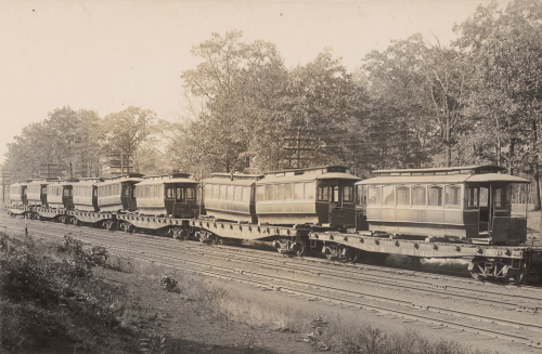 A long line of flat, roofless train cars with streetcars on them.