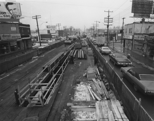 Installed decking on middle lanes of Yonge Street with traffic on either side. Storefronts line both side of road. Construction materials lie on decking.