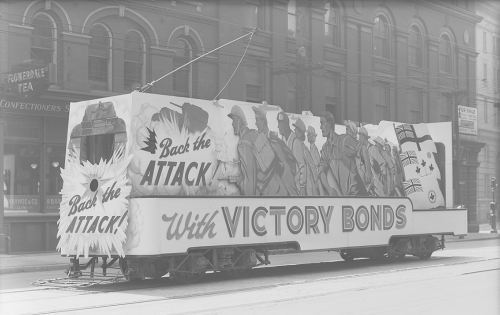 Victory Bonds sign attached to TTC vehicle. Background shows brick building storefronts.