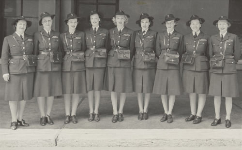 Group of nine women in uniform with hats and over the shoulder bags.